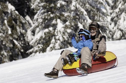 Young woman and child sliding down in inflatable snow tube